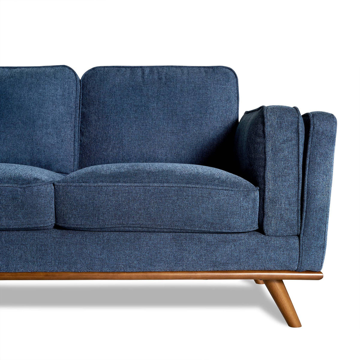 The Maddox Sectional, with its blue fabric upholstery and mid-century modern style, features wooden legs and armrests. Set against a white background, its plush cushions bring elegance to any living room. The focus is on the right half of this minimalist design.