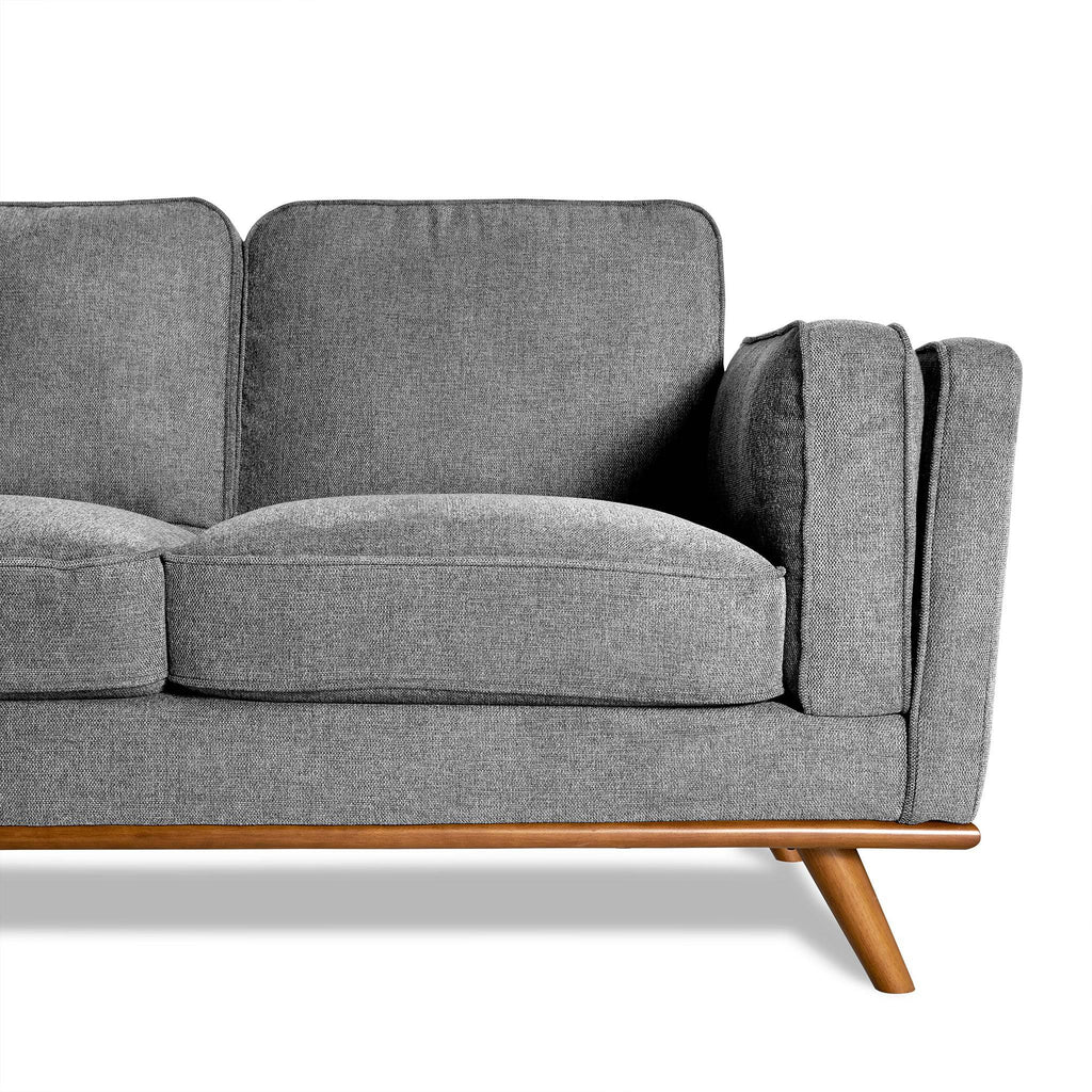 The Maddox is a modern gray fabric sofa with a wooden base and angled legs. It features plush cushions and an armrest, embodying mid-century modern design against a white background, perfect for any living room.
