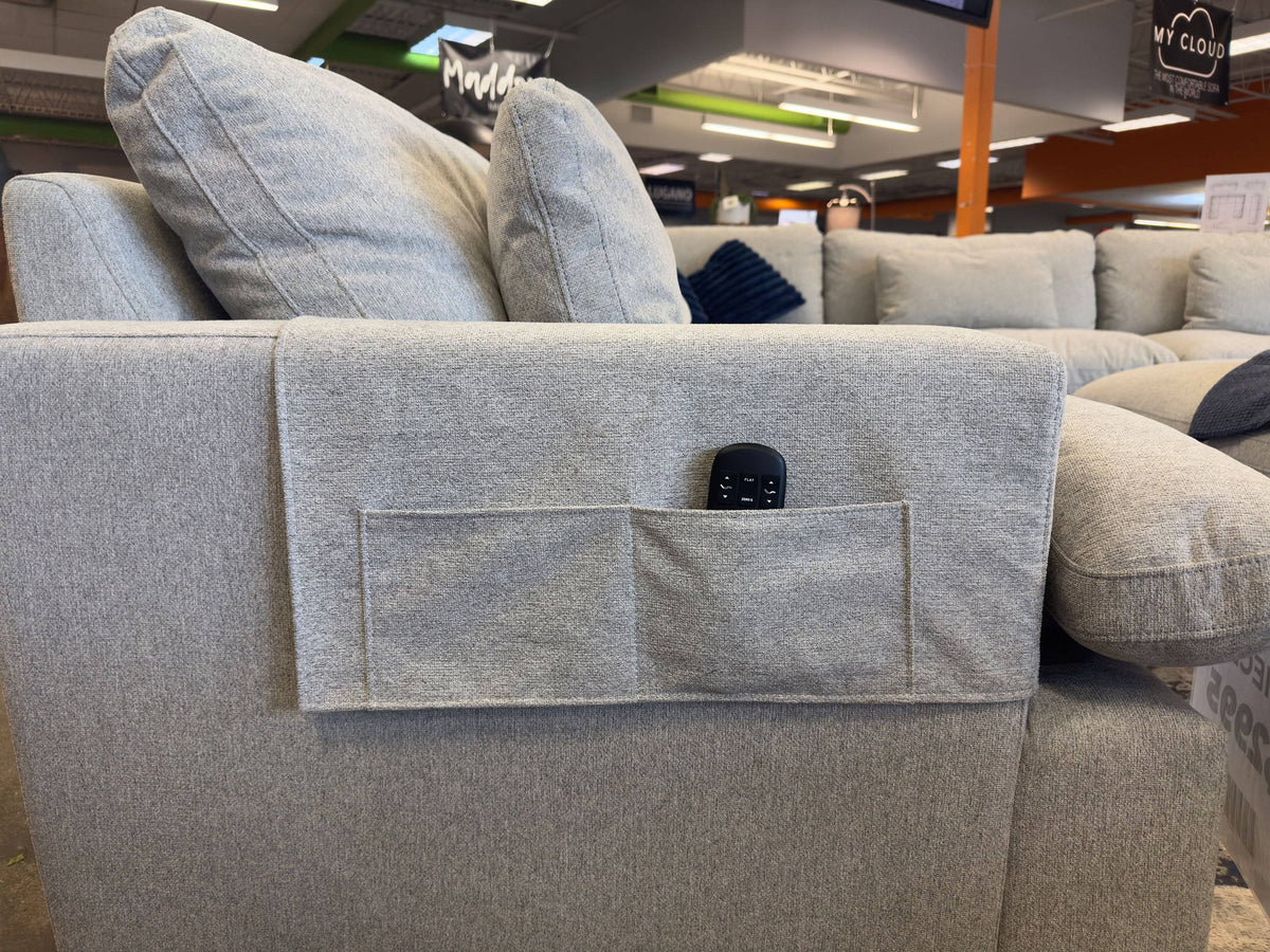 A light gray sofa, featuring My Cloud Arm Covers and a fabric pocket ideal for a remote control, is displayed in a furniture store along with other couches.