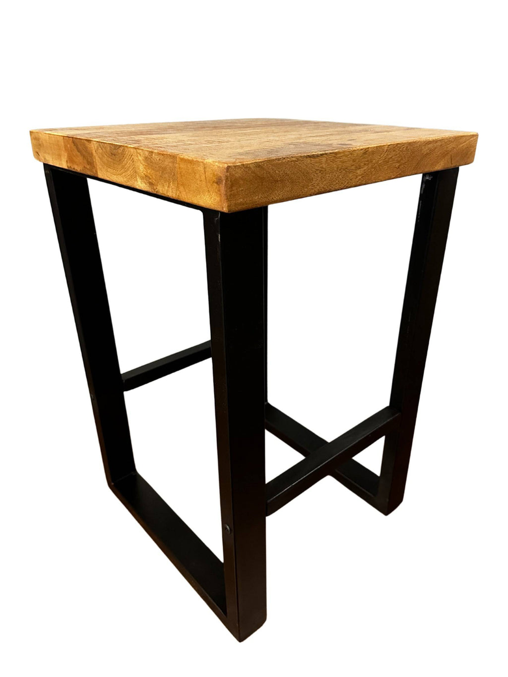The Mango Stool features a square sustainable mango wood top and black metal legs forming a geometric frame. Its minimalist design contrasts natural wood grain with sleek industrial metal, making it perfect as an accent piece in modern spaces.